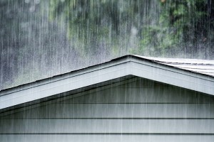 Drenching June summer rain storm downpour pounding and splattering water on a grimy old backyard clapboard siding shed roof.
